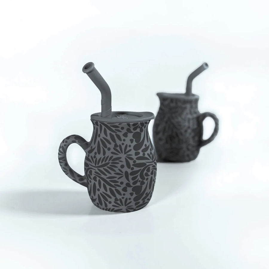 Two black ceramic mugs with straw holders on a white background