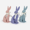Three pastel-colored rabbit figurines with white bows on a white background