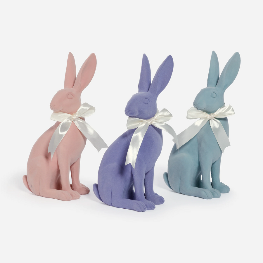 Three pastel-colored rabbit figurines with white bows on a white background