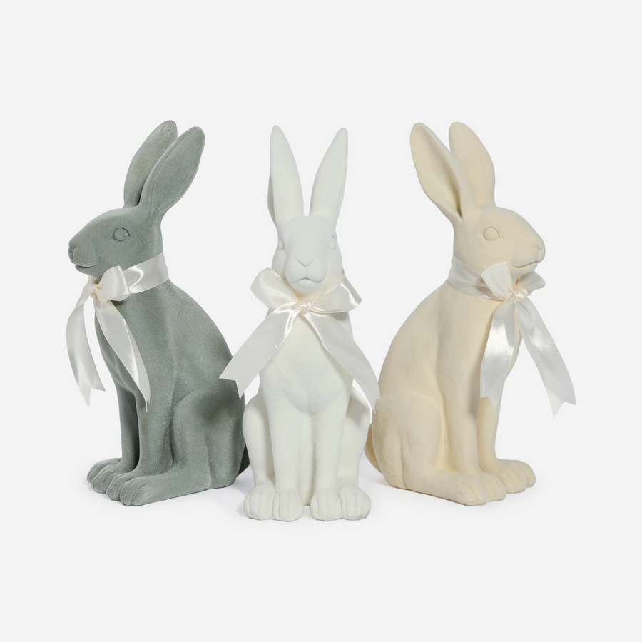 Three decorative rabbits in gray, white, and beige with white ribbons on a white background