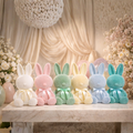 Pastel-colored bunny plush toys on a marble surface with floral decorations in the background.