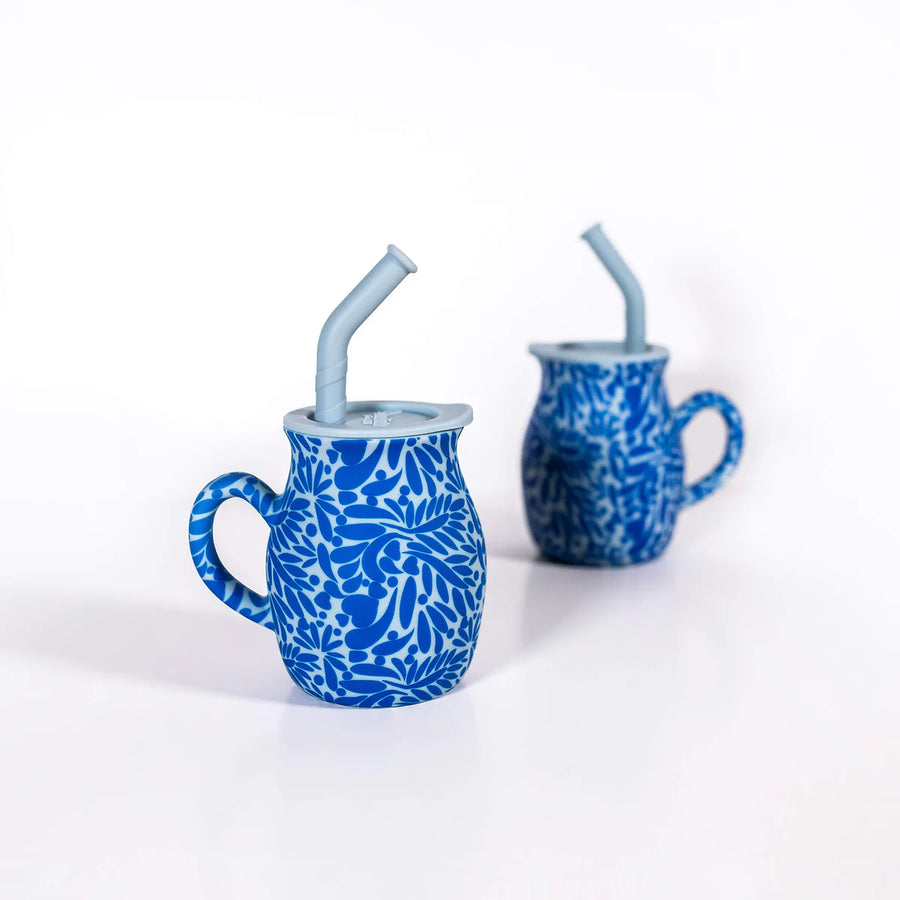 Two blue silicone talavera mugs with floral patterns and straws on a white background
