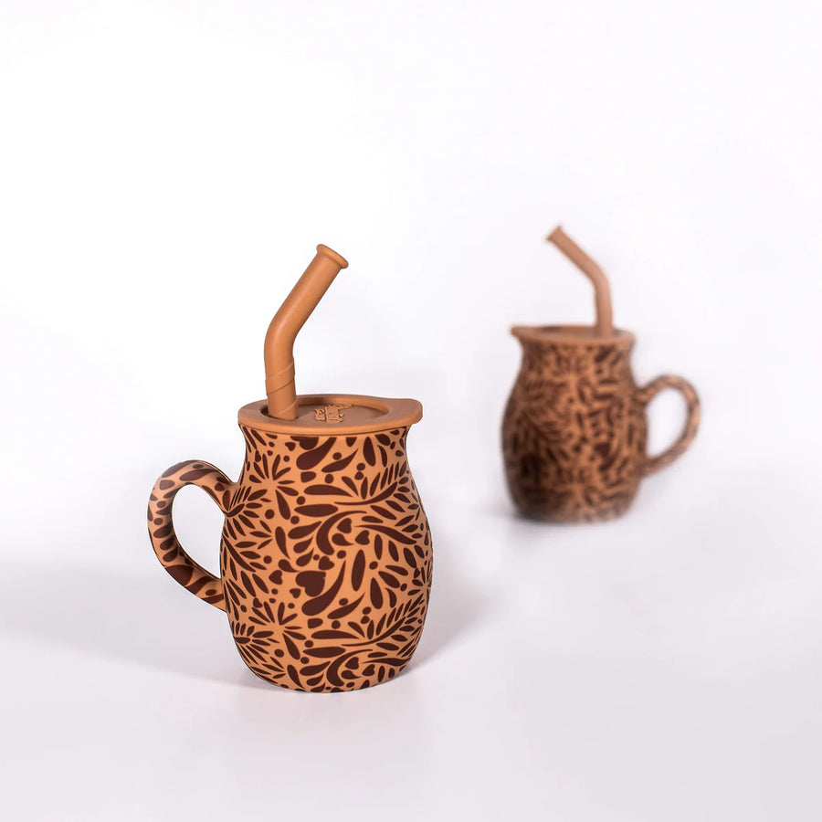 Two brown ceramic mugs with unique patterns and straws on a white background