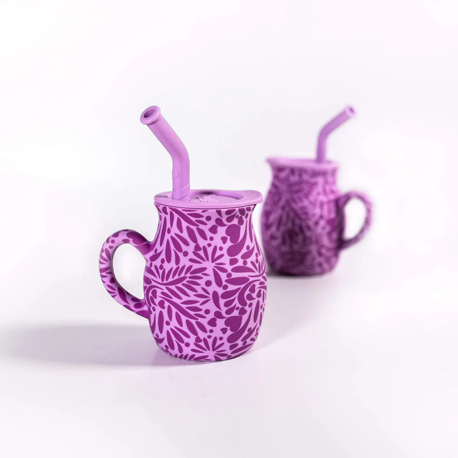 Two purple silicone talavera mugs with floral patterns and straws on a white background