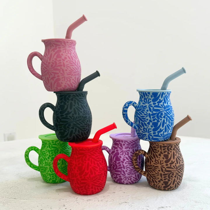 Stack of colorful talavera silicone mugs with straws on a white surface
