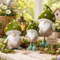 Three gnome figurines with green hats and white beards in a garden setting with flowers and a lantern.