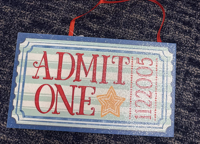 Blue Admit One ticket ornament with blue scalloped border, mint and white stripes, red ADMIT ONE, gold star and number 1122005