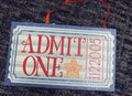 Blue Admit One ticket ornament with blue scalloped border, mint and white stripes, red ADMIT ONE, gold star and number 1122005