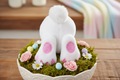 White plush bunny with pink accents on a bed of moss and flowers in a decorative bowl.