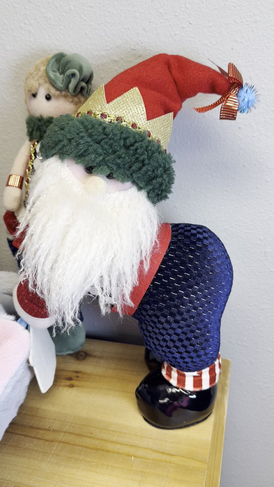 Little standing Santa Claus plush figure with fluffy white beard, red crown-band hat and navy checkered pants